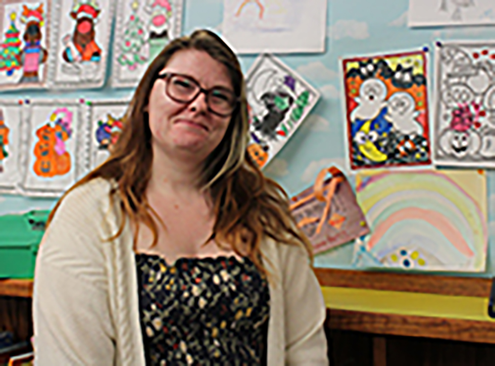 A photo of Kaela in front of a library bulletin board filled with children's coloring pages